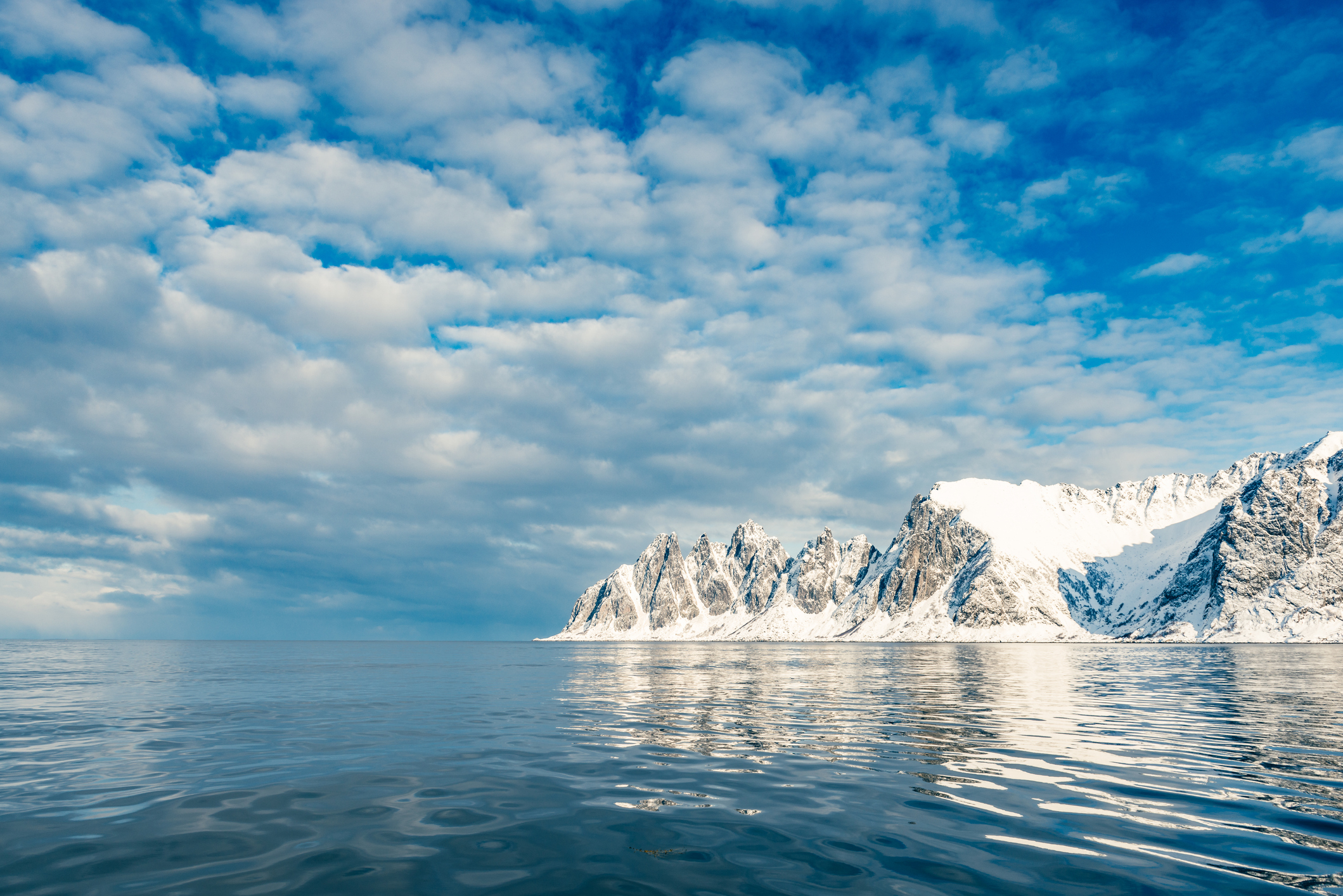 Snow covered mountains, blue skye and calm sea. Senja, Norway.